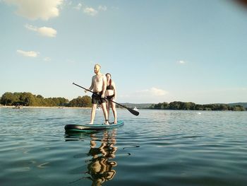 Friends standing on paddleboard in lake against sky