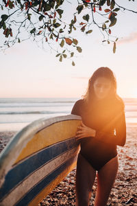 Mature woman carrying surfboard at beach during sunset