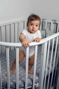 One year old child in white clothes standing in a white round bed in his nursery