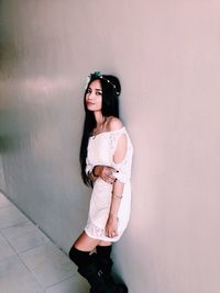 Portrait of beautiful woman wearing white dress and tiara against wall