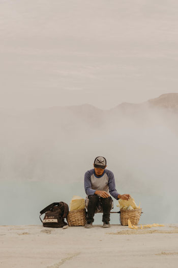 FULL LENGTH OF MAN SITTING AGAINST MOUNTAIN