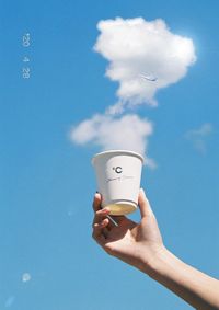 Human hand holding coffee cup against blue sky