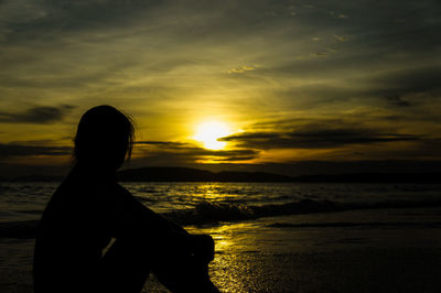 Silhouette woman on beach against sky during sunset
