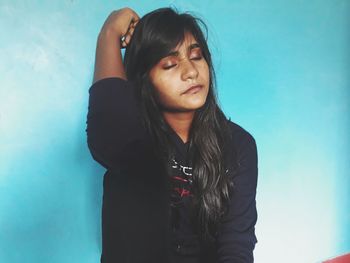 Young woman looking away while standing against blue wall