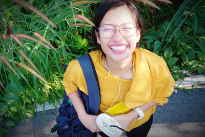 High angle portrait of smiling young woman standing against plants