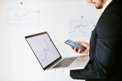 Midsection of businessman holding laptop and mobile phone at office