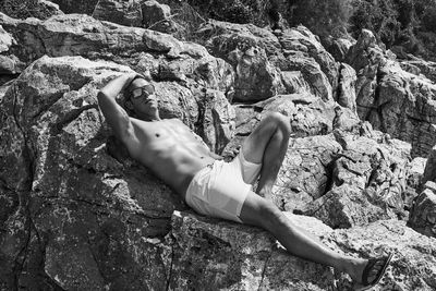 Portrait of shirtless mid adult man relaxing on rock during sunny day