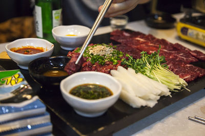 Midsection of person holding meat with chopsticks above food in tray