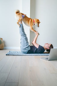 Full length of woman playing with dog while lying on floor