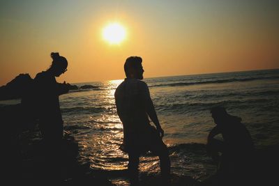 Silhouette people standing on beach against orange sky