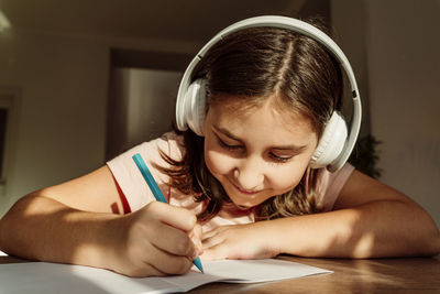 Smiling girl wearing wireless headphones writing in book at desk