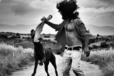 Man playing with dog on field against sky