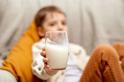 Little adorable boy sitting on the couch at home and drinking milk. fresh milk in glass