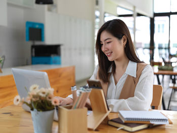 Smiling young businesswoman using laptop while sitting at cafe