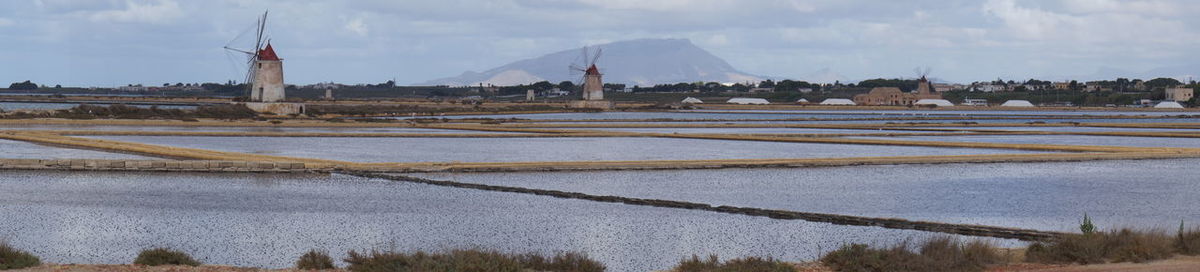 Traditional windmill at lakeshore against sky