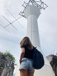 Low angle view of woman standing by communications tower against sky