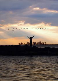 Silhouette man flying over sea against sky during sunset