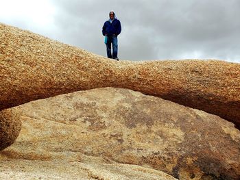 Rear view of man standing on rock against sky