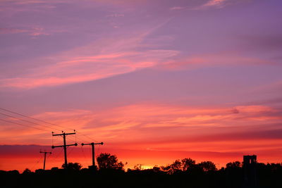 Silhouette trees and electricity pylon against romantic sky at sunset