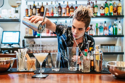 Serious barman pouring fresh alcohol cocktail in glass goblet placed on counter in bar