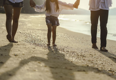Low section of parents holding daughter hand while walking at beach