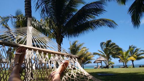 Low section of woman relaxing on hammock at beach against blue sky