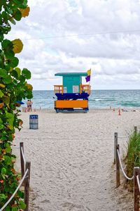 Lifeguard hut on shore at beach against cloudy sky