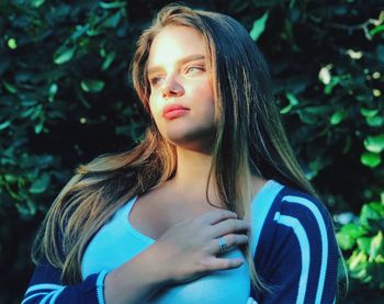 Beautiful young woman looking away against trees