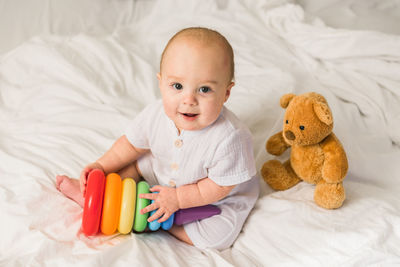 Portrait of cute baby boy with teddy bear on bed at home