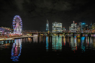 Illuminated city by river against sky at night