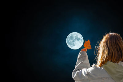 Rear view of woman holding globe against black background