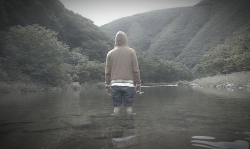 Rear view of man standing on lake against mountain