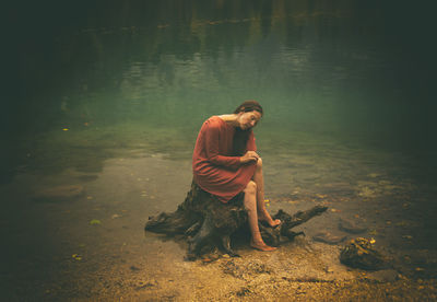 Woman in orange dress sitting on a log on the shore of a lake, italy ii