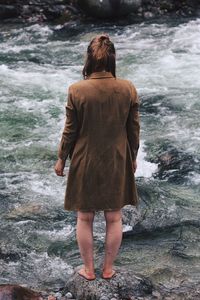 Rear view of woman standing on rock by sea