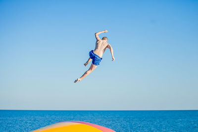 Rear view of shirtless man jumping in sea against sky