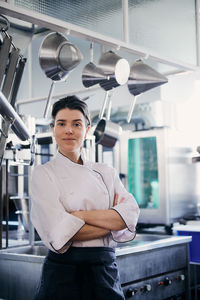 Portrait of mid adult female chef standing arms crossed in commercial kitchen