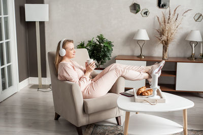 Full length of woman holding coffee cup sitting on armchair