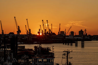 Cranes at commercial dock against sky during sunset