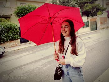 Young woman holding umbrella while standing on road in rain