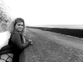 Portrait of young woman sitting on beach against clear sky