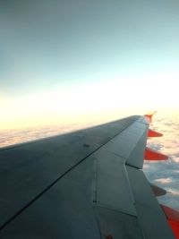 Airplane wing over sea against sky during sunset