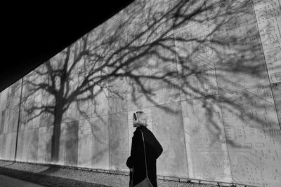 Rear view of person standing by bare tree in city