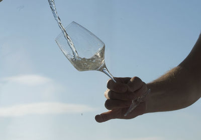 Low angle view of man holding glass against sky