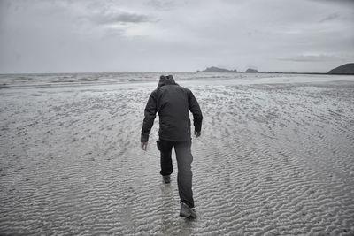 Rear view of man walking at beach against sky