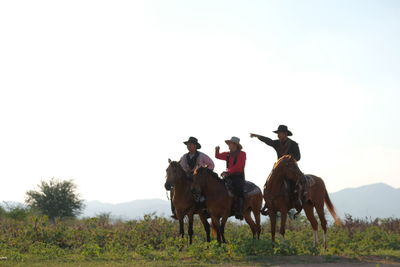 People riding horses on field against sky