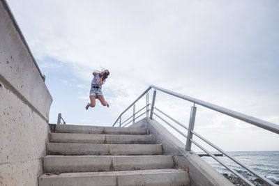 Full length of woman jumping on staircase against sky