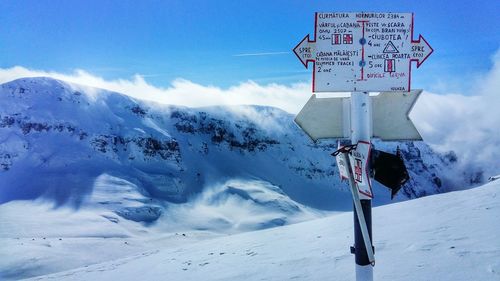 Information sign on snowcapped mountains against sky