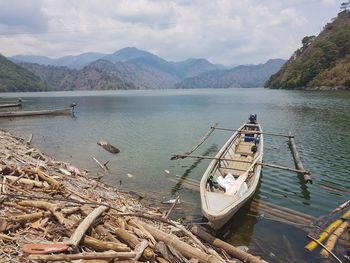 Fishing boats moored on sea by mountains against sky