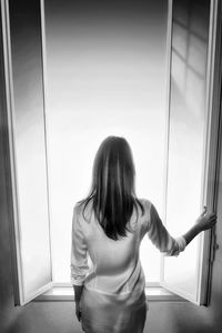 Rear view of mid adult woman looking through window at home