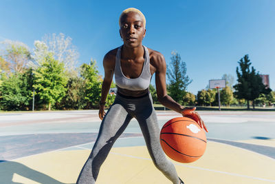 Confident sportswoman playing basketball in sports court